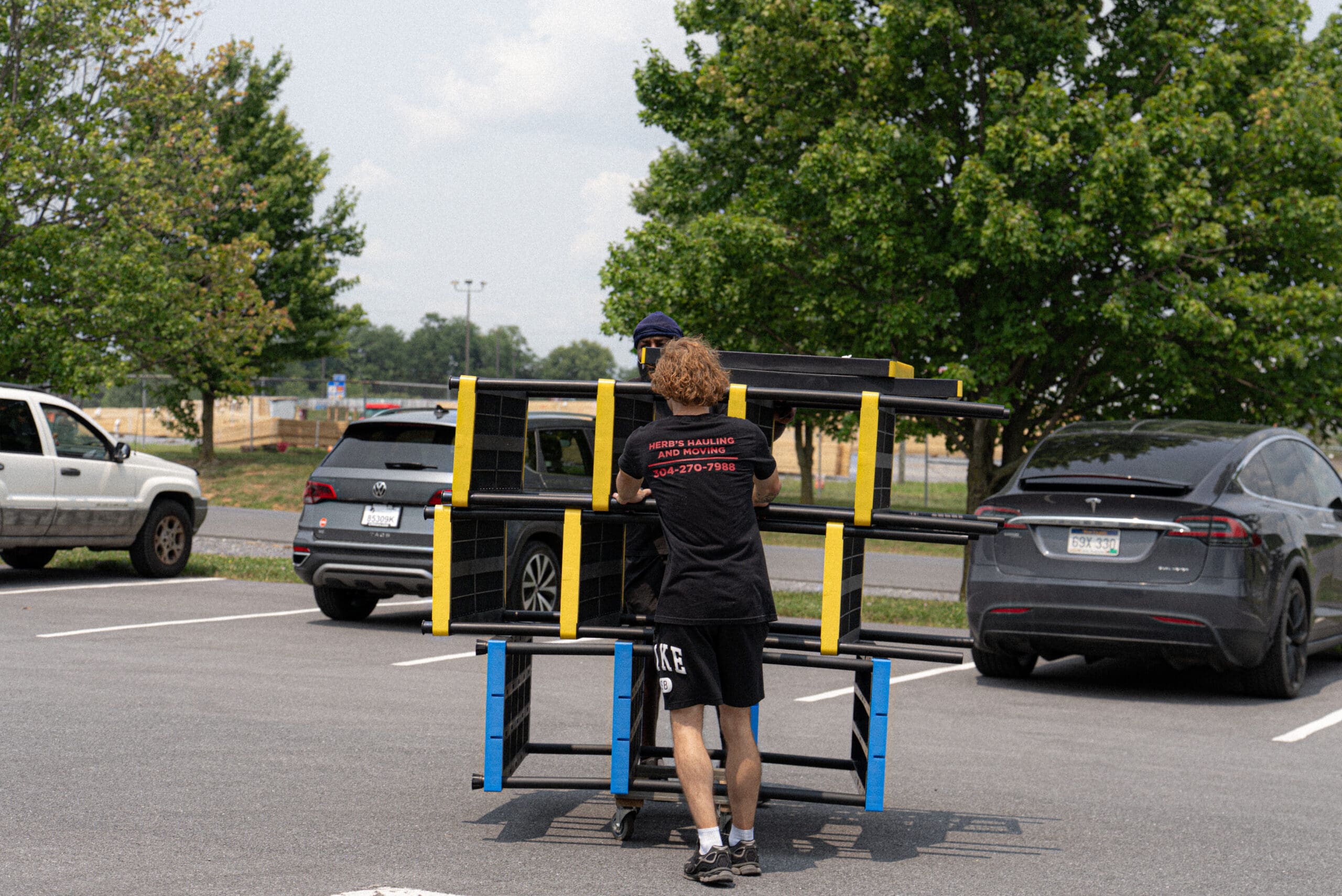 A person operates a yellow and blue portable arcade game machine in a parking lot on a clear day.